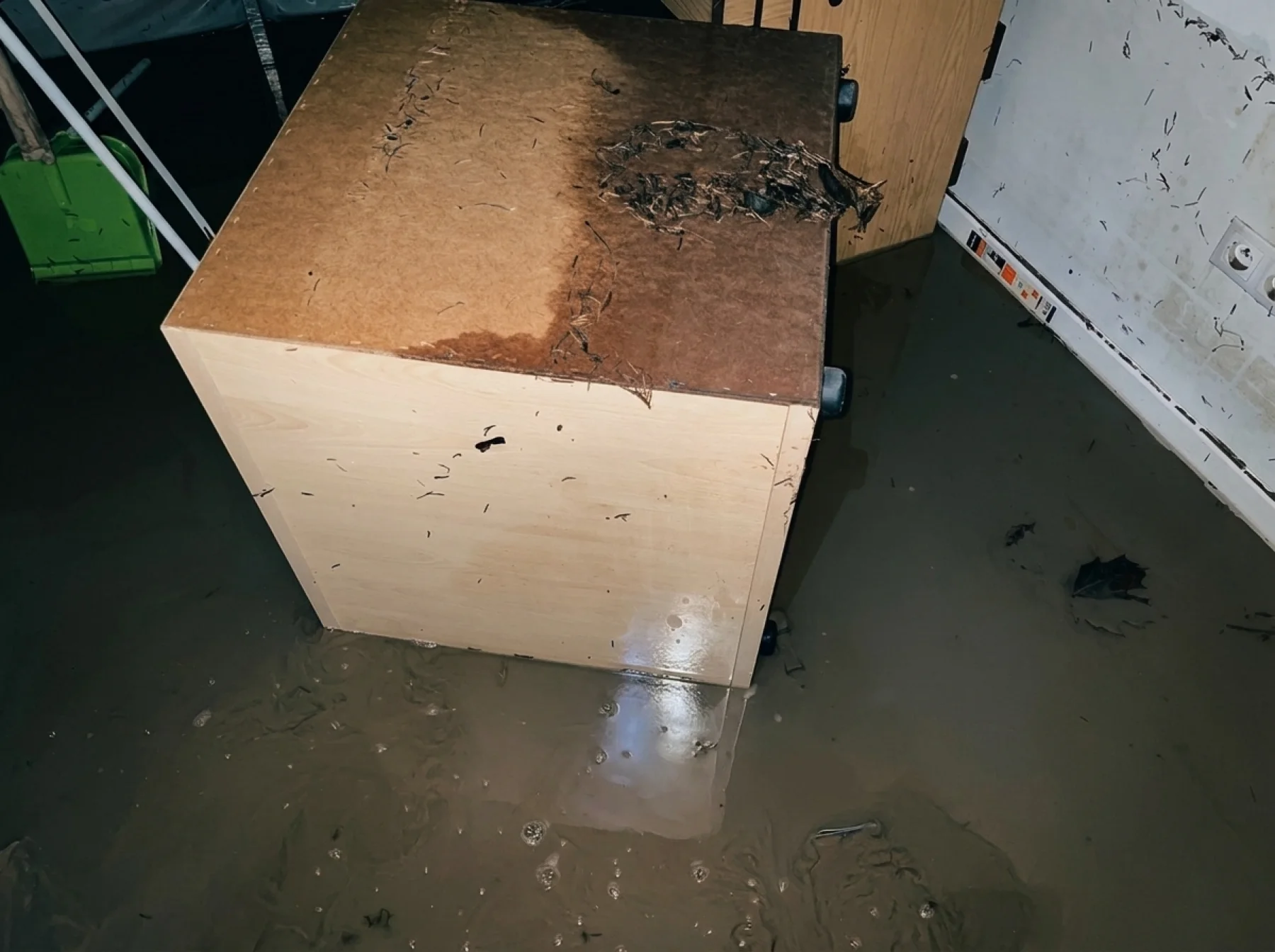 Furniture and drawers standing in brown floodwater, debris floating on the surface.